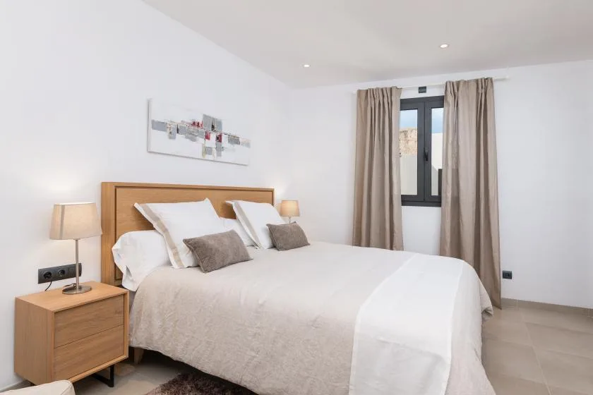 A bright bedroom with a neatly made bed and a window framed by curtains.