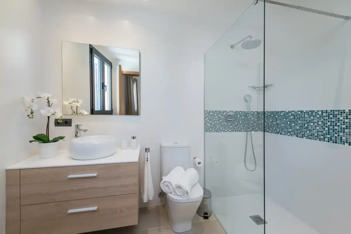 A bright bathroom with a wood vanity and glass shower.