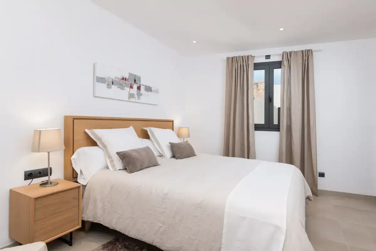 A bright bedroom features a double bed and a window with curtains.