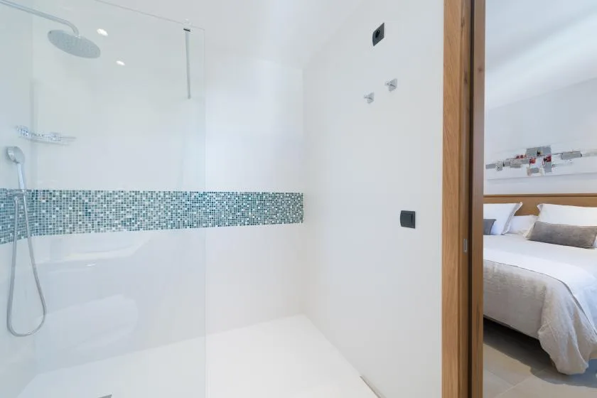 A white shower area with a glass screen and a patterned tile strip.