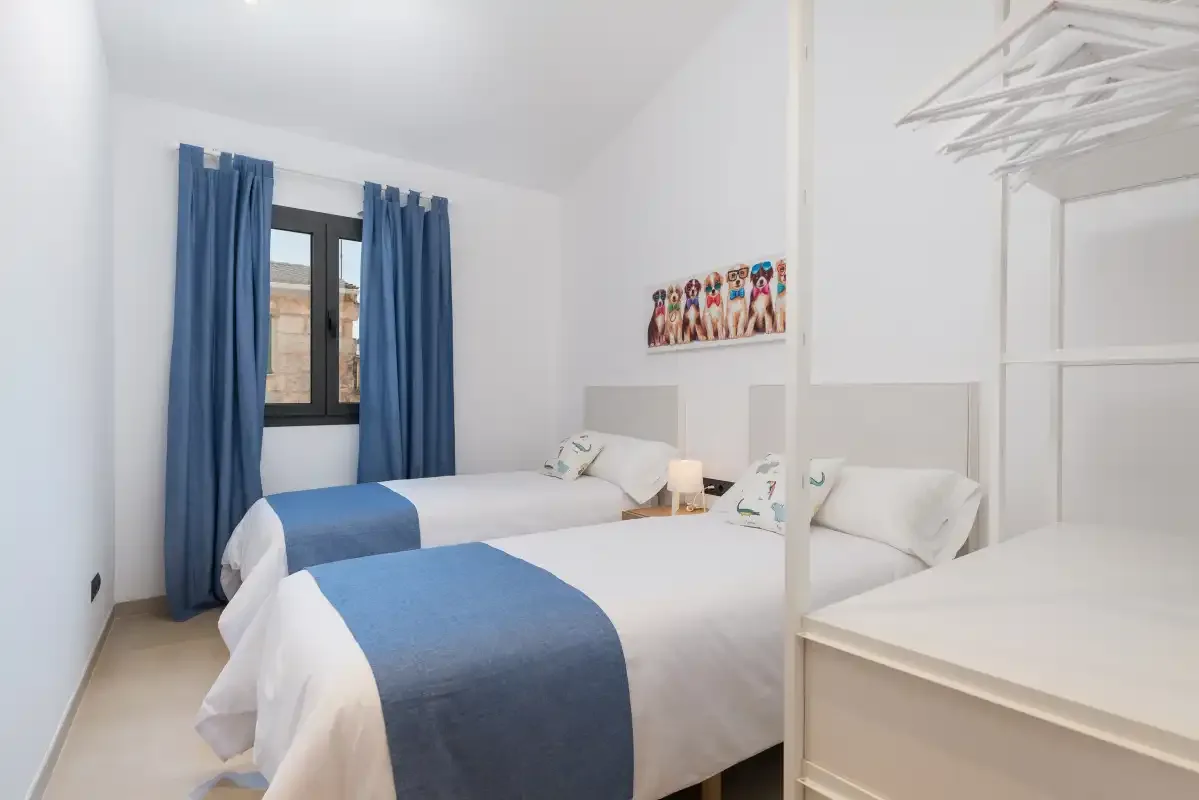 A bright bedroom with white bedding, blue runners, and blue curtains.