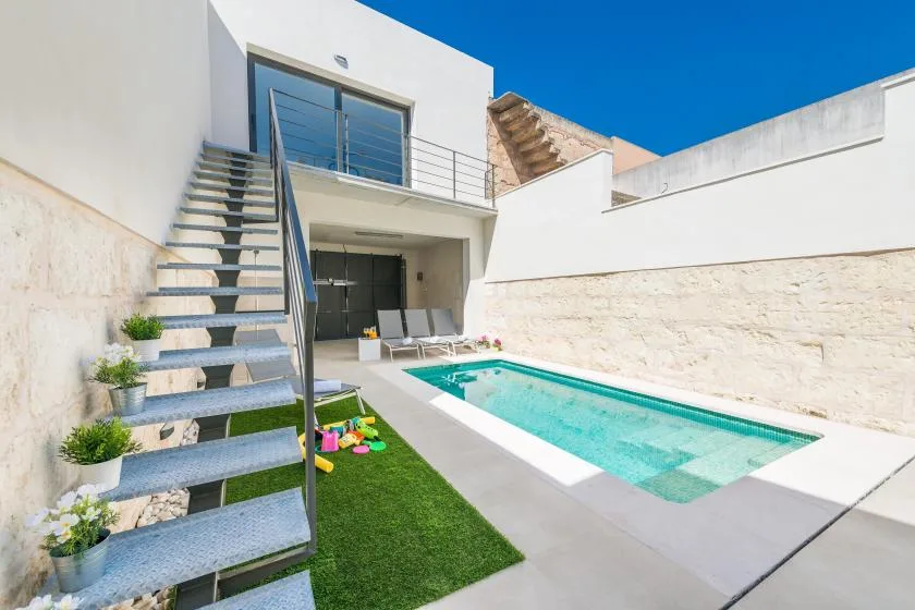 A small outdoor pool beside a modern white house and an exterior staircase.