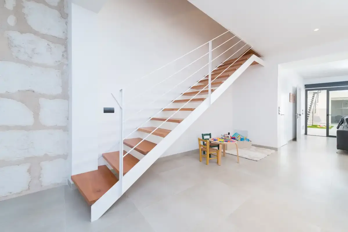 A bright interior shows a staircase with wooden steps and white railings.