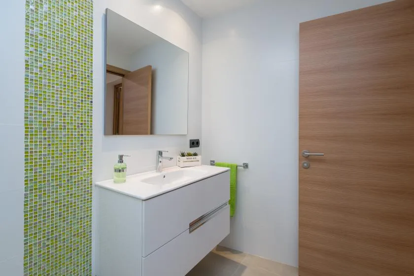 A bathroom with a white sink vanity, wall mirror, and wood-finish door.