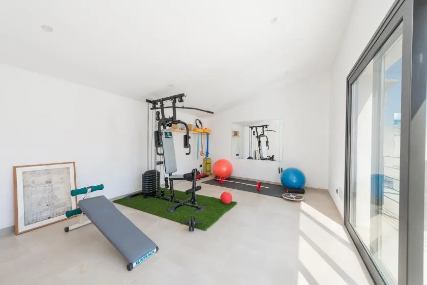 A bright home gym with exercise equipment, a workout bench, and large windows.