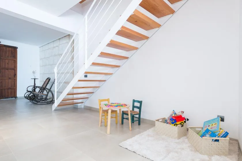 A bright interior with a staircase, small table, and children’s toys.