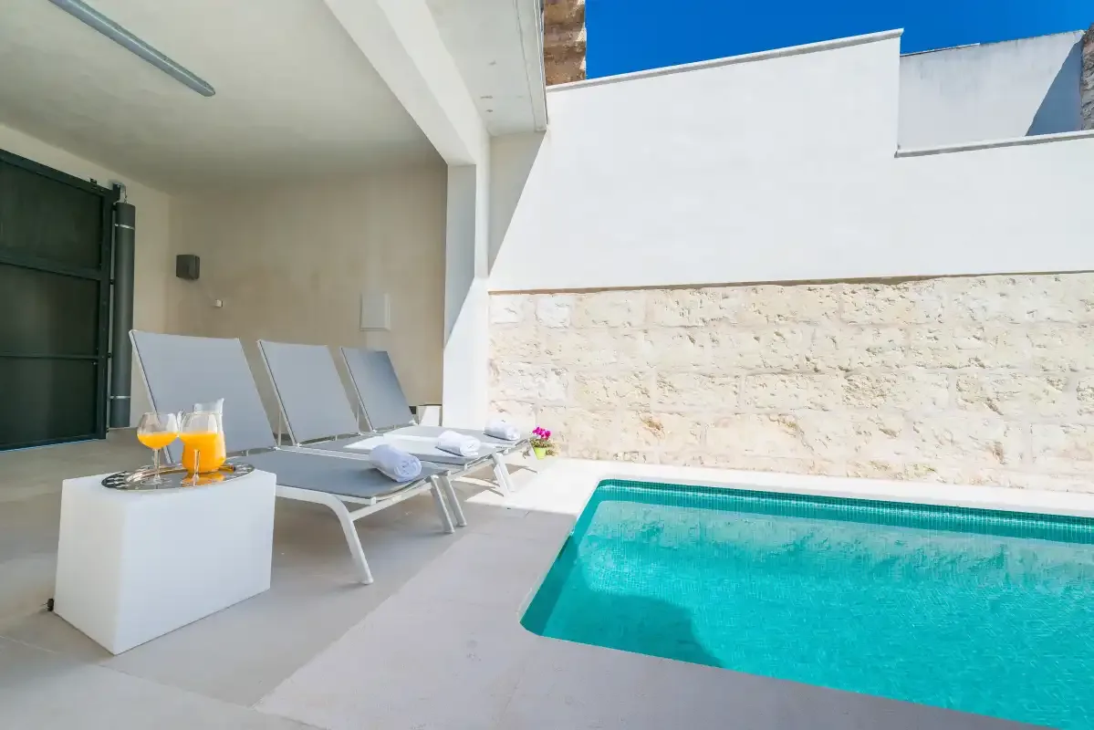 A sunlit patio with a small swimming pool and lounge seating.