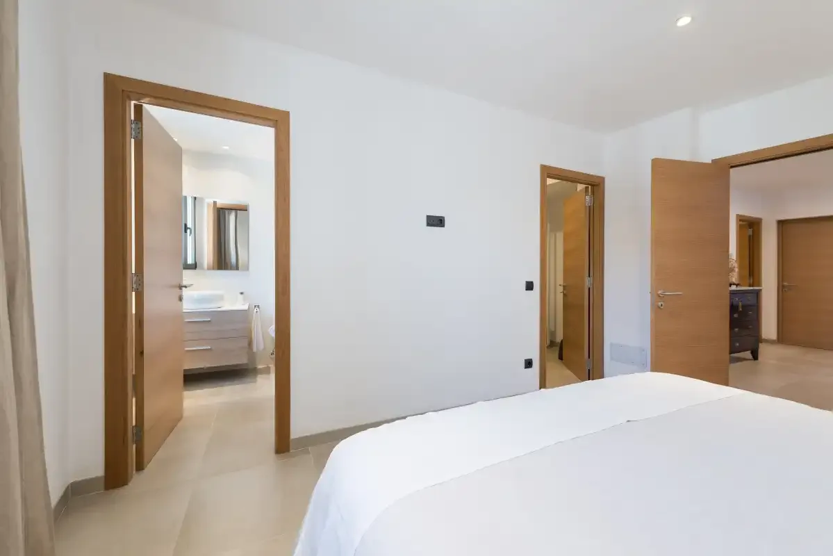 A bedroom with a white bed and open wooden doors.