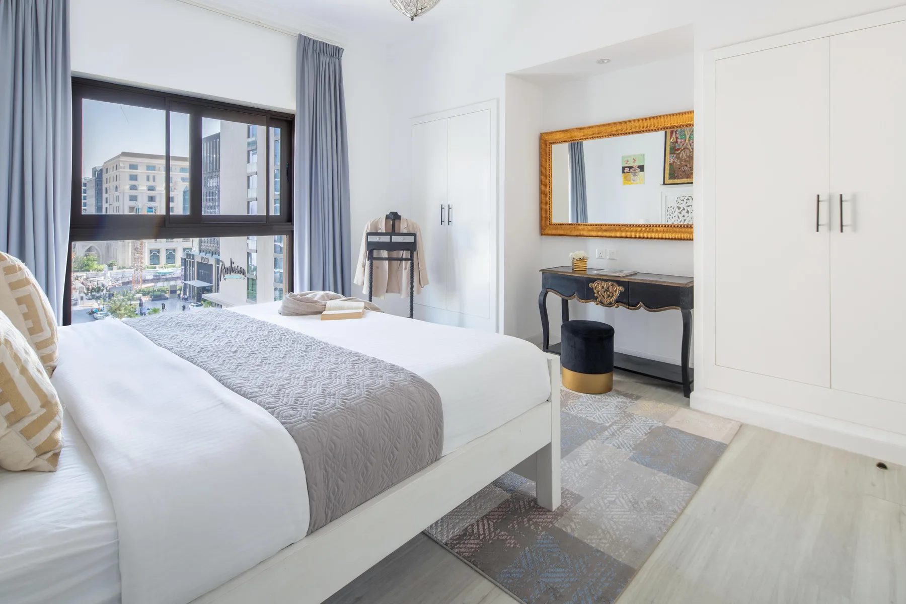 Un dormitorio luminoso con una cama, una ventana amplia y un escritorio pequeño.