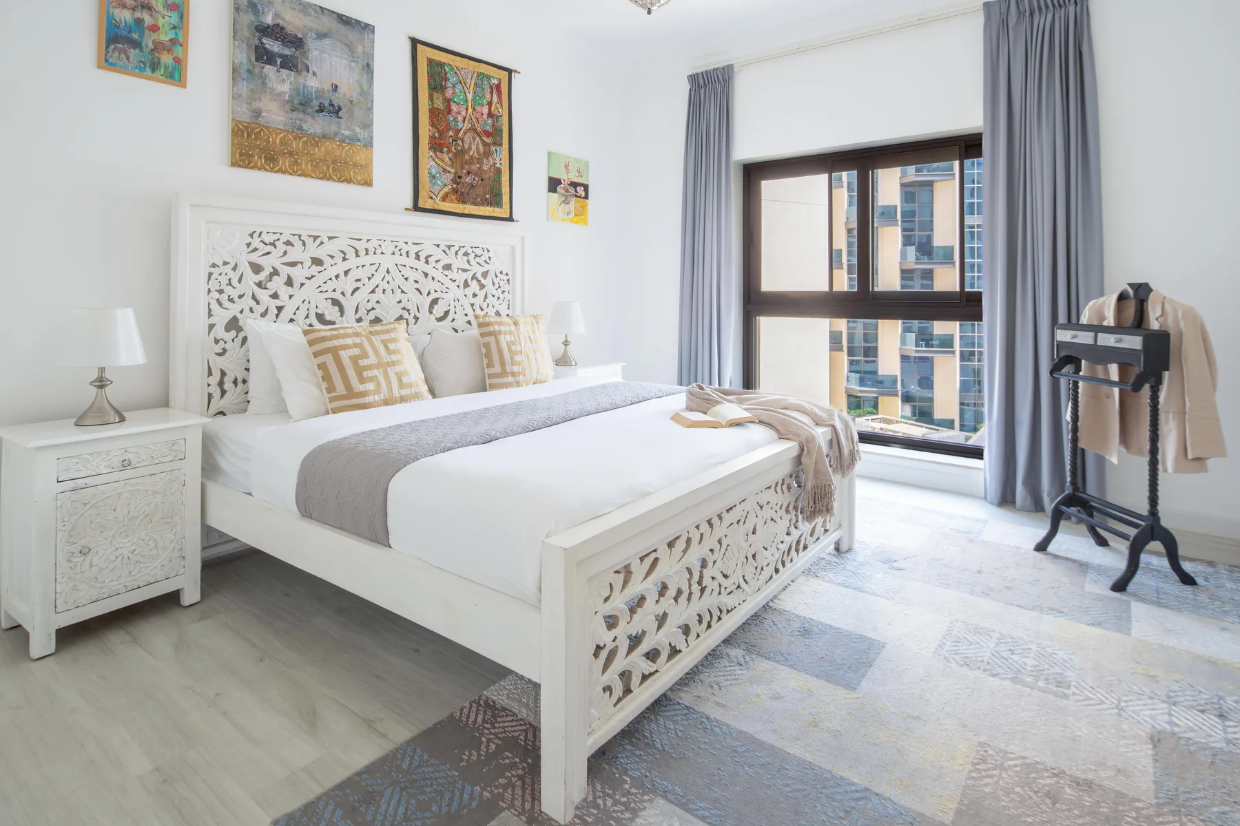 Un dormitorio luminoso con una cama blanca, cuadros decorativos y una ventana grande.