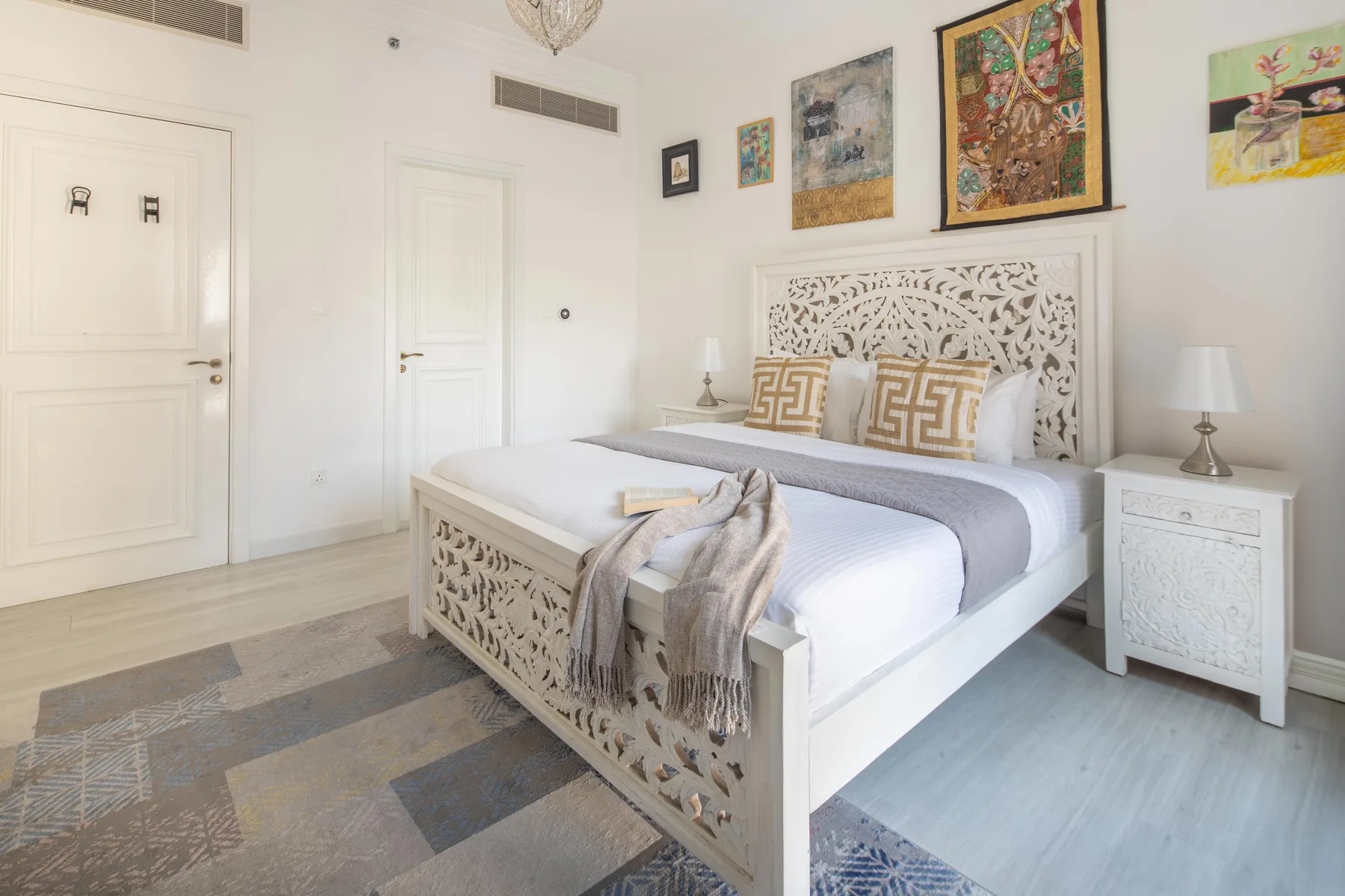 Un dormitorio luminoso con una cama blanca y cuadros sobre el cabecero.