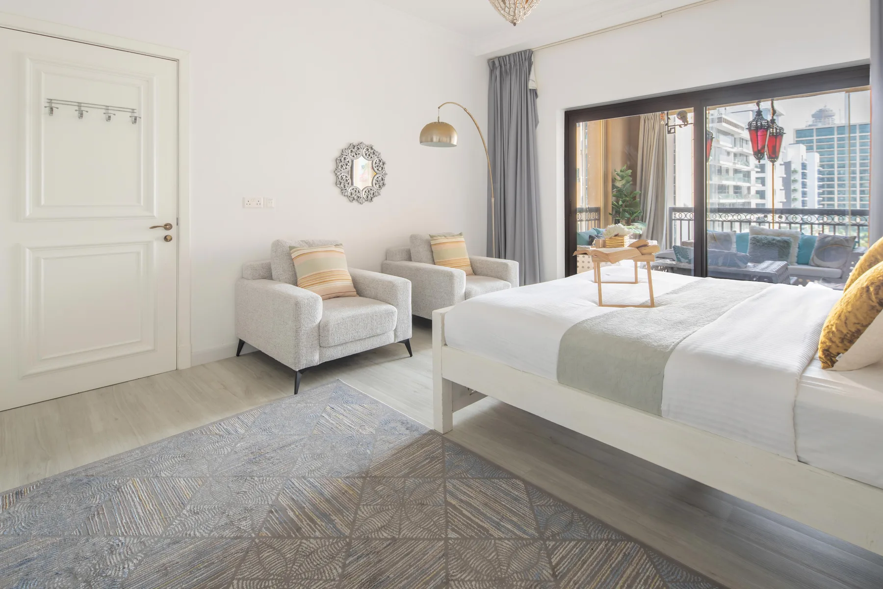 Un dormitorio luminoso con una cama, dos sillones y grandes ventanas con vistas a la ciudad.