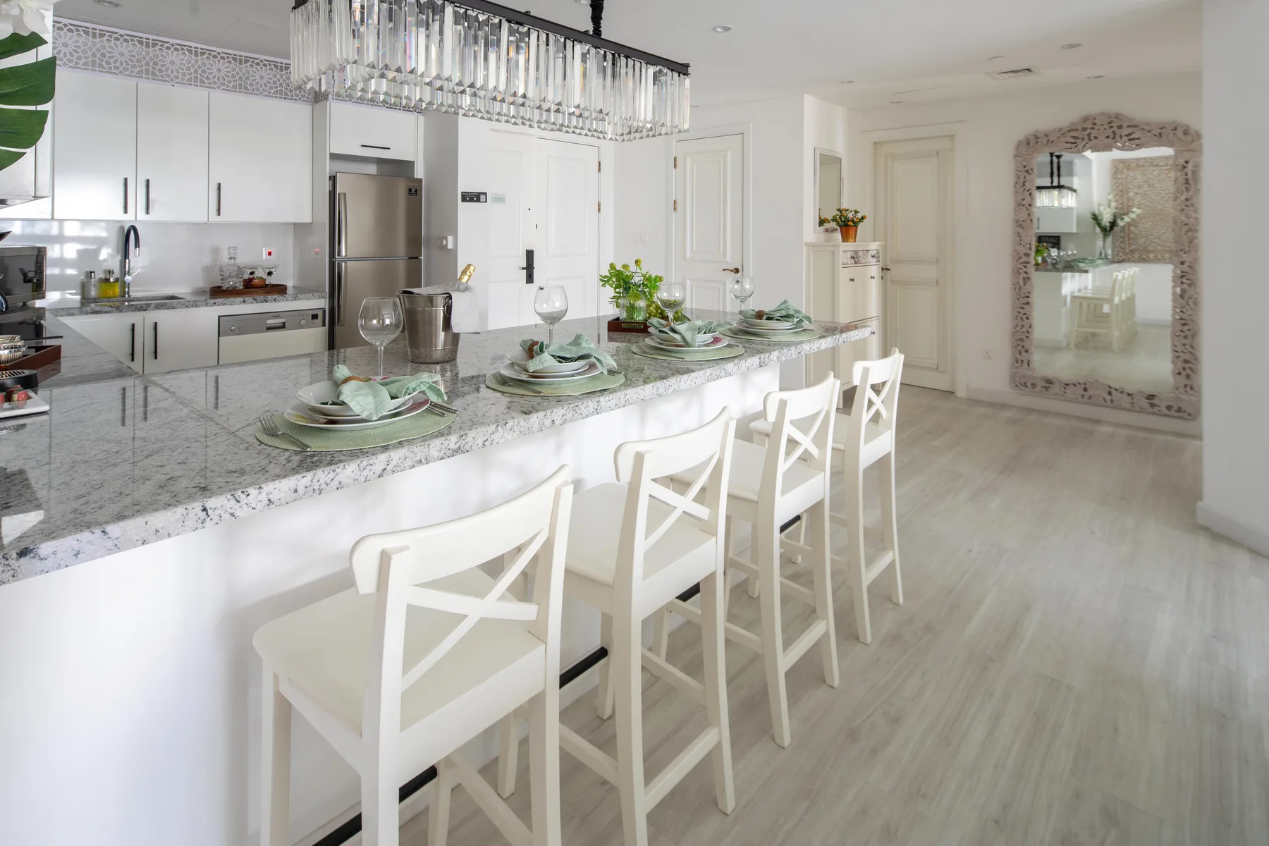 Una cocina luminosa con una isla larga, asientos blancos y una lámpara colgante.