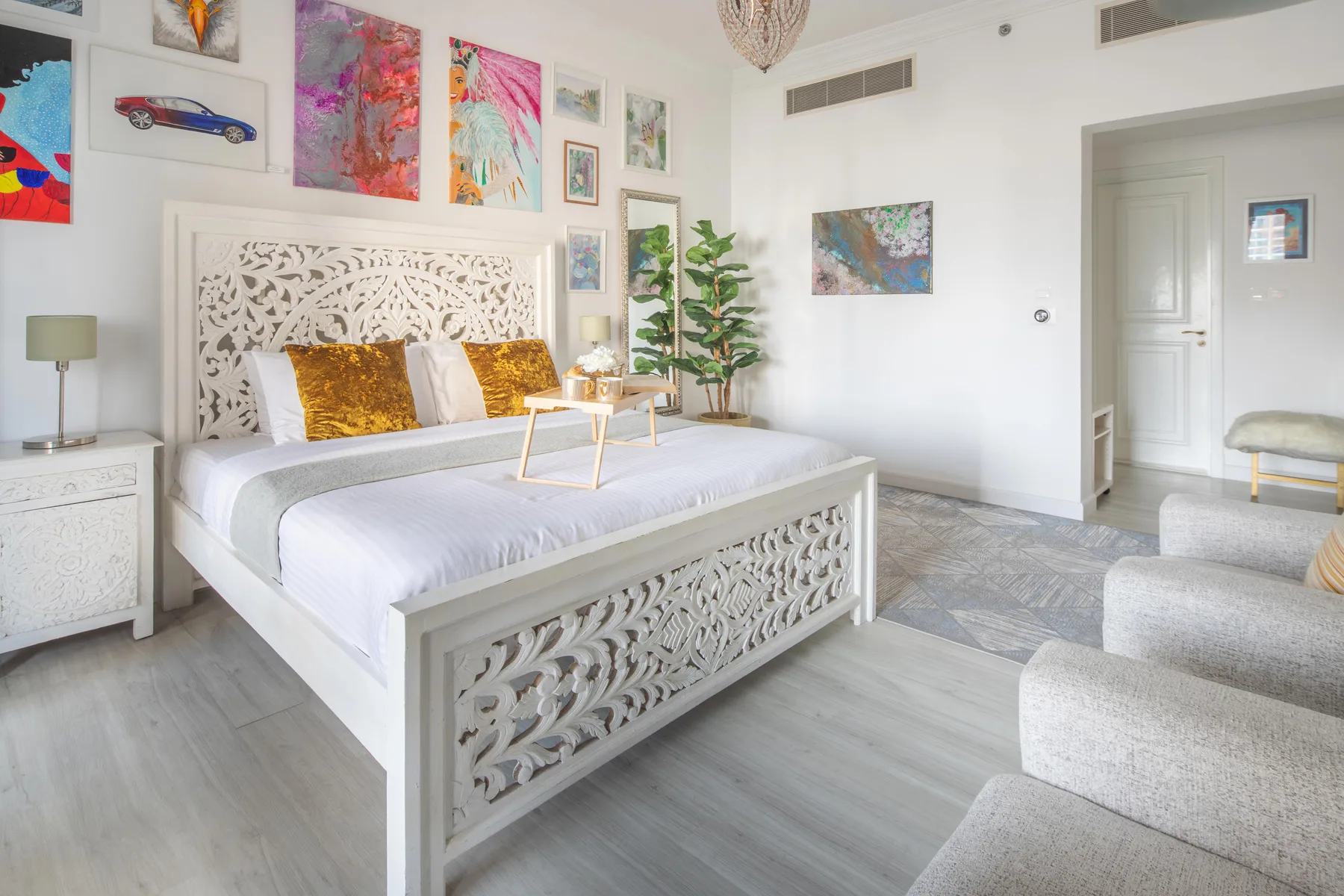 Un dormitorio luminoso con una cama blanca tallada y obras de arte coloridas en las paredes.