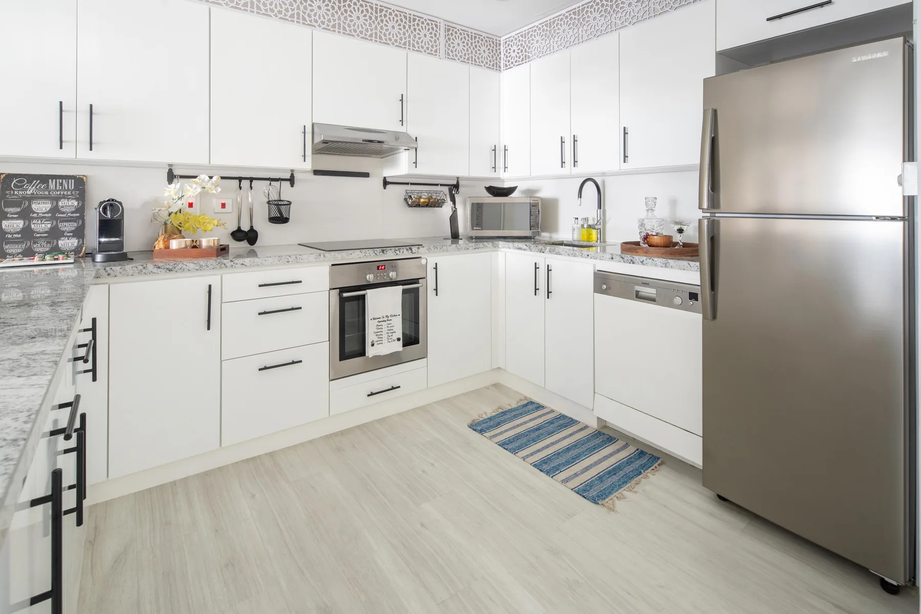 Una cocina moderna y luminosa con gabinetes blancos, electrodomésticos de acero inoxidable y una alfombra a rayas.
