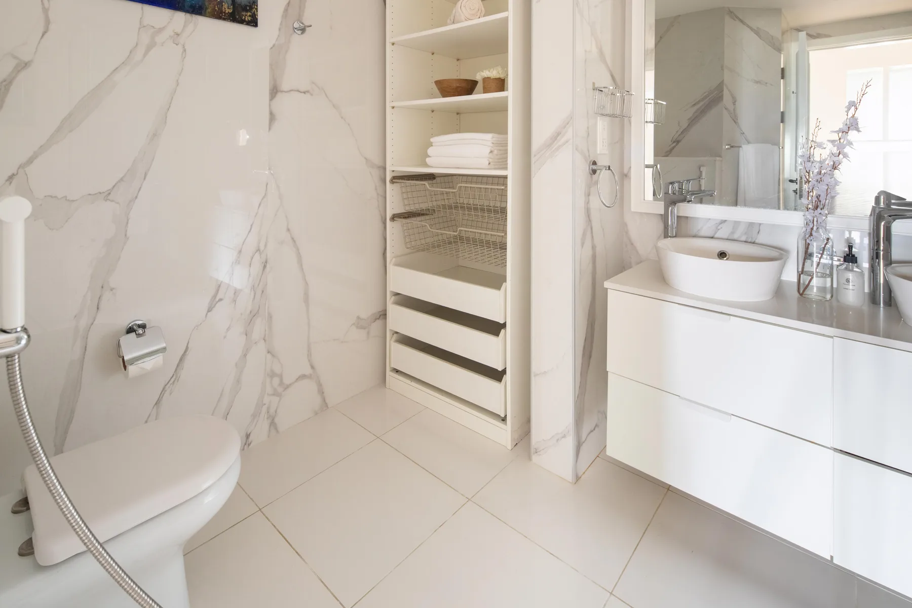 Un baño luminoso con inodoro, lavabo y estanterías abiertas.