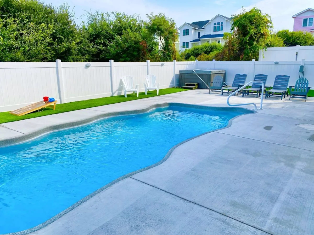 Una piscina al aire libre junto a un patio pavimentado con asientos.