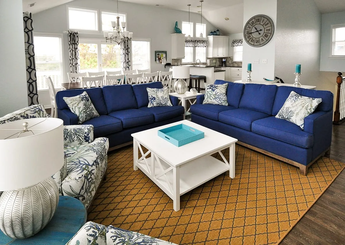 Una sala de estar con asientos azules alrededor de una mesa de centro blanca.