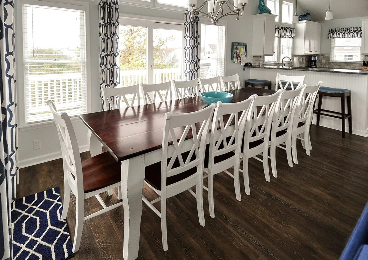 Comedor con una mesa larga y asientos blancos junto a una cocina luminosa.