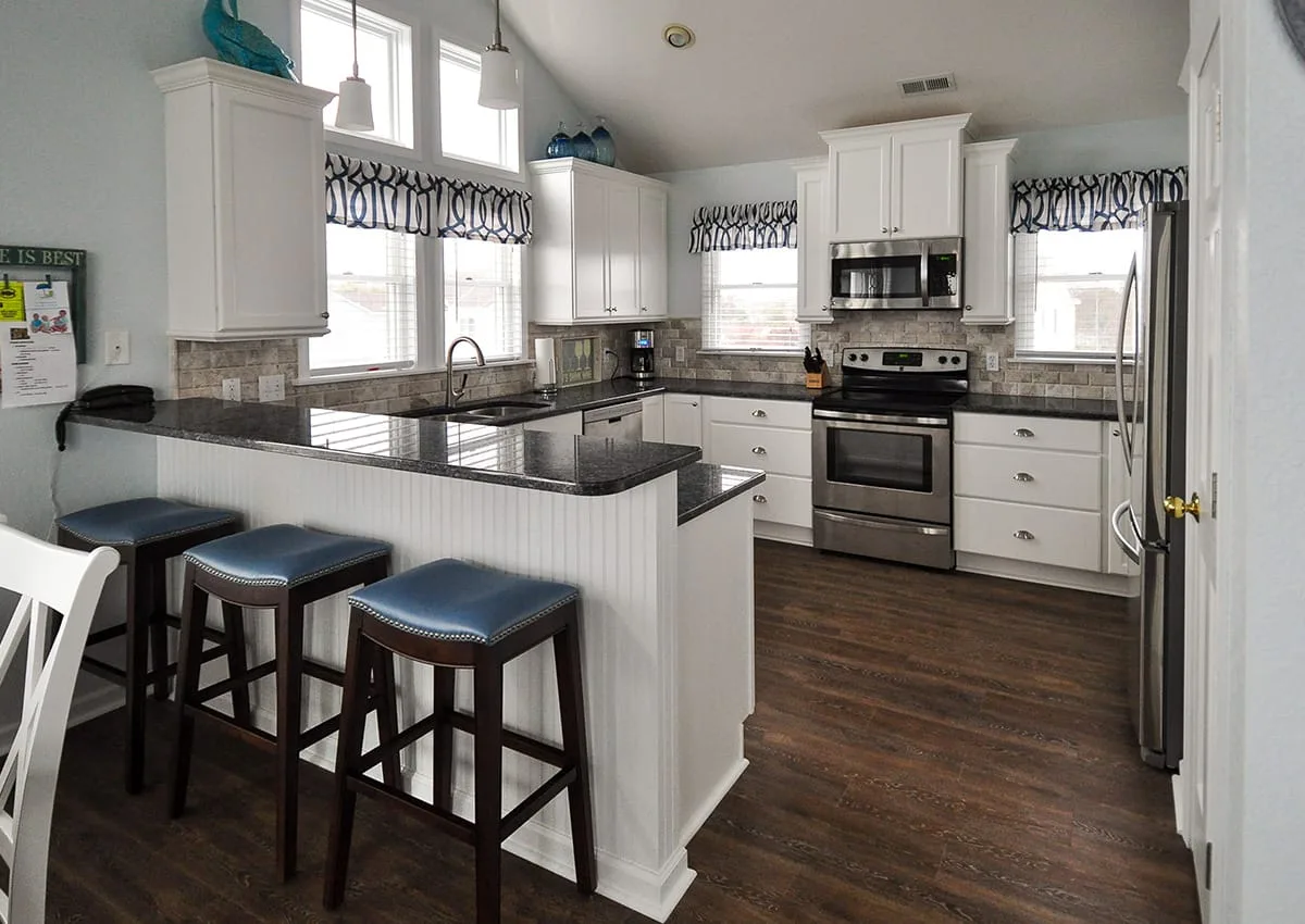 A bright kitchen with white cabinets, dark countertops, and a breakfast bar.