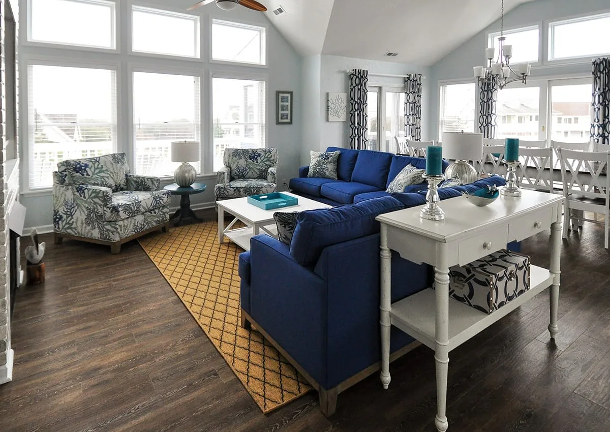 A bright living room with blue seating, a white coffee table, and large windows.