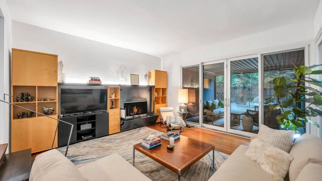 Una sala luminosa con televisor, chimenea y puertas de vidrio que dan a un patio.
