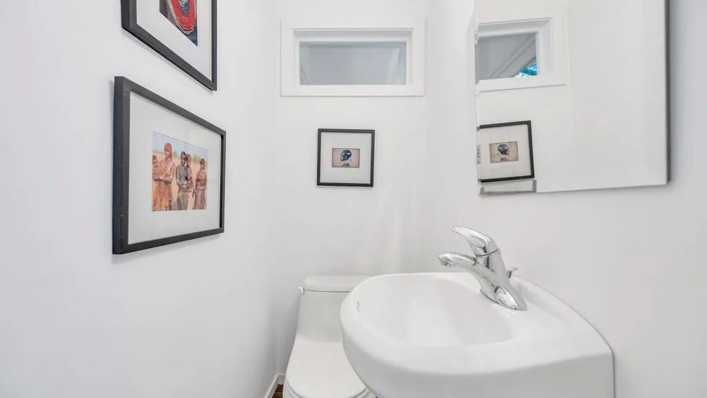 Un lavabo y un inodoro están bajo cuadros enmarcados y un espejo de pared.