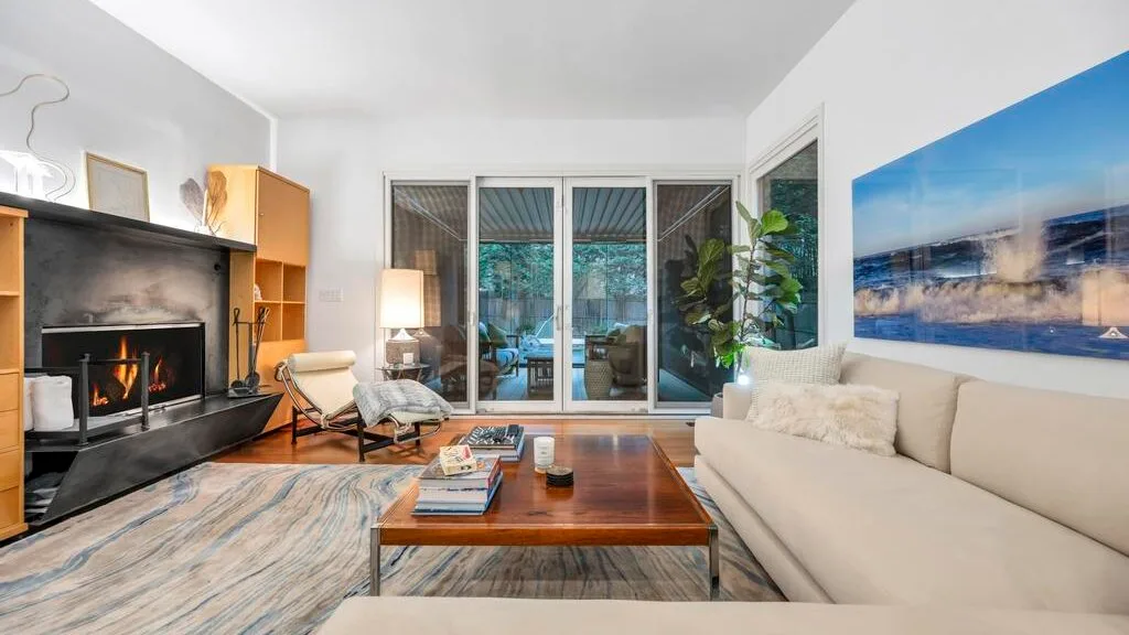 Una sala luminosa con chimenea, asientos y puertas de vidrio que dan a un balcón.