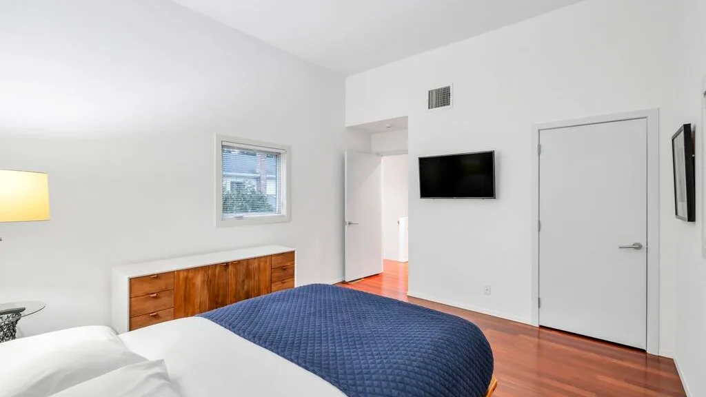 Un dormitorio con una cama cubierta por una manta azul y un televisor en la pared.