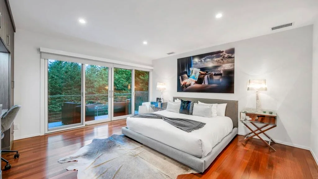 Un dormitorio luminoso con una cama grande junto a puertas corredizas de vidrio.
