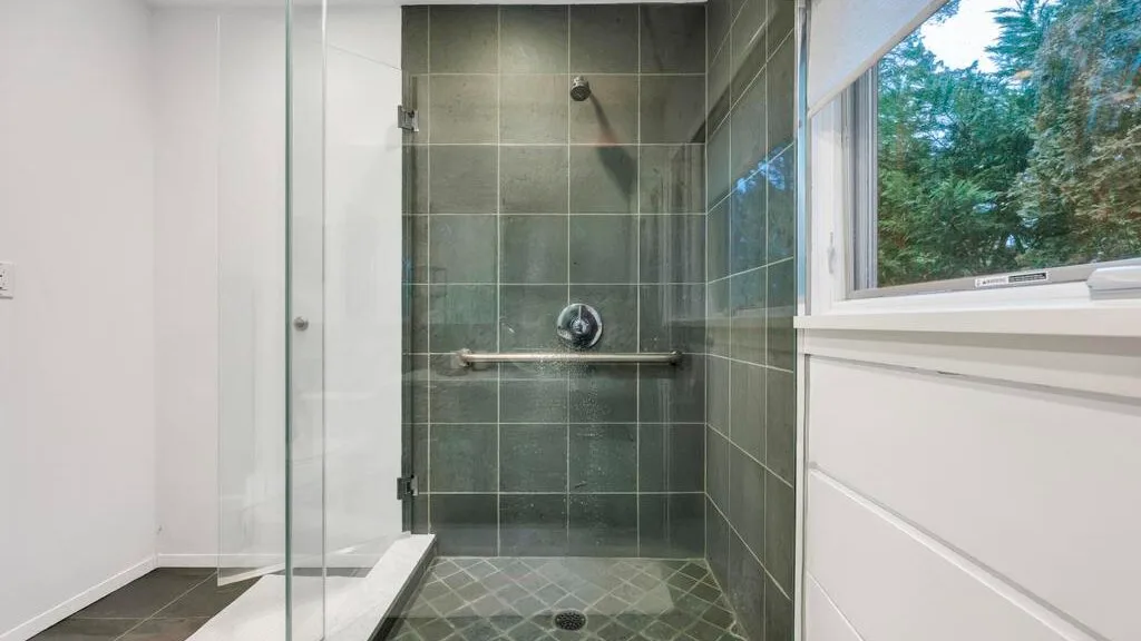 Una ducha de azulejos con paneles de vidrio está junto a una ventana grande.