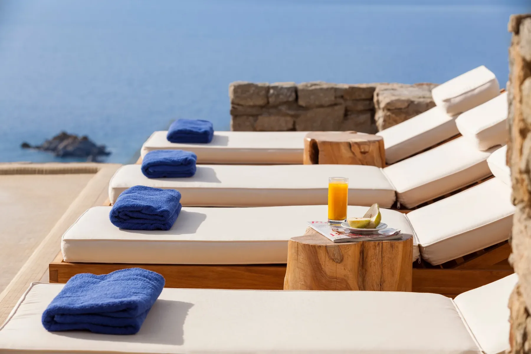 Outdoor lounge area with cushioned sun loungers and folded blue towels beside the water.