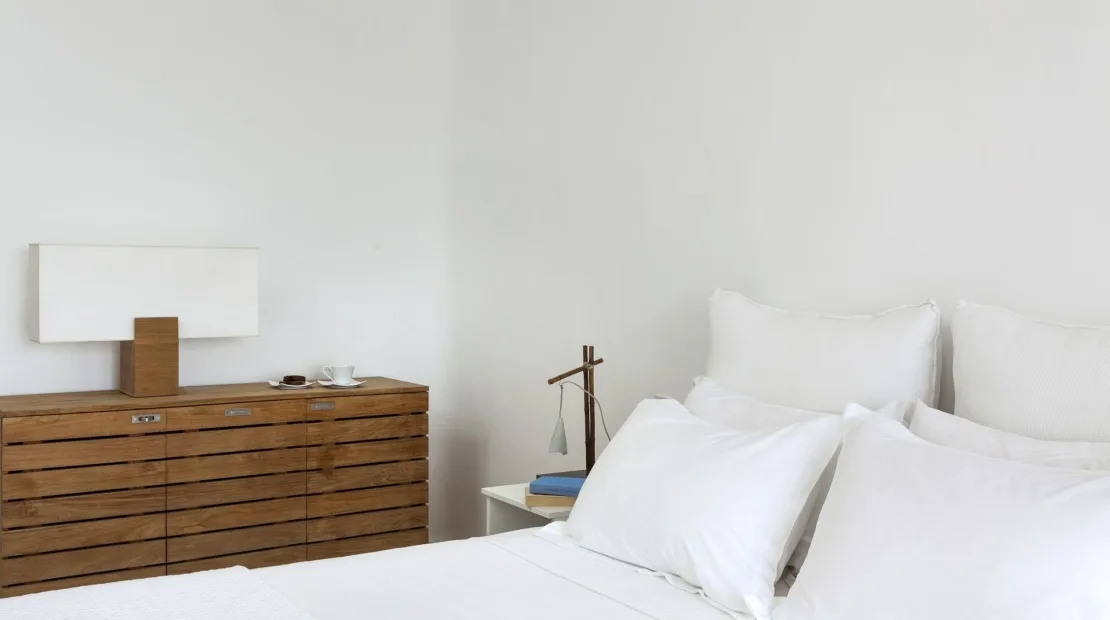 A bright bedroom with white bedding and a wooden dresser.