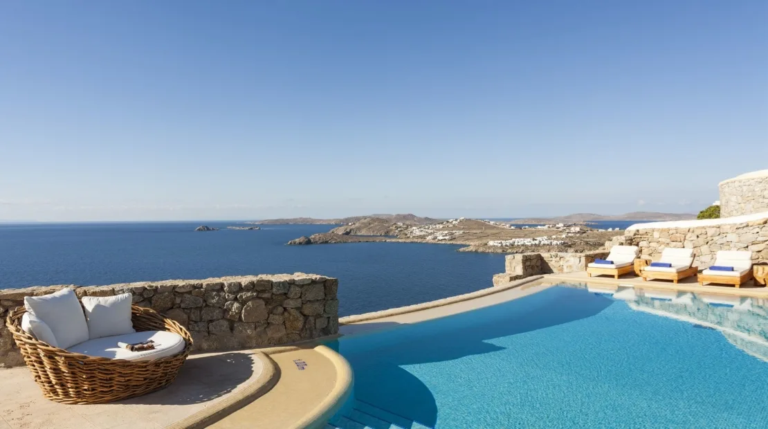 A swimming pool overlooks the sea, with cushioned seating beside the water.