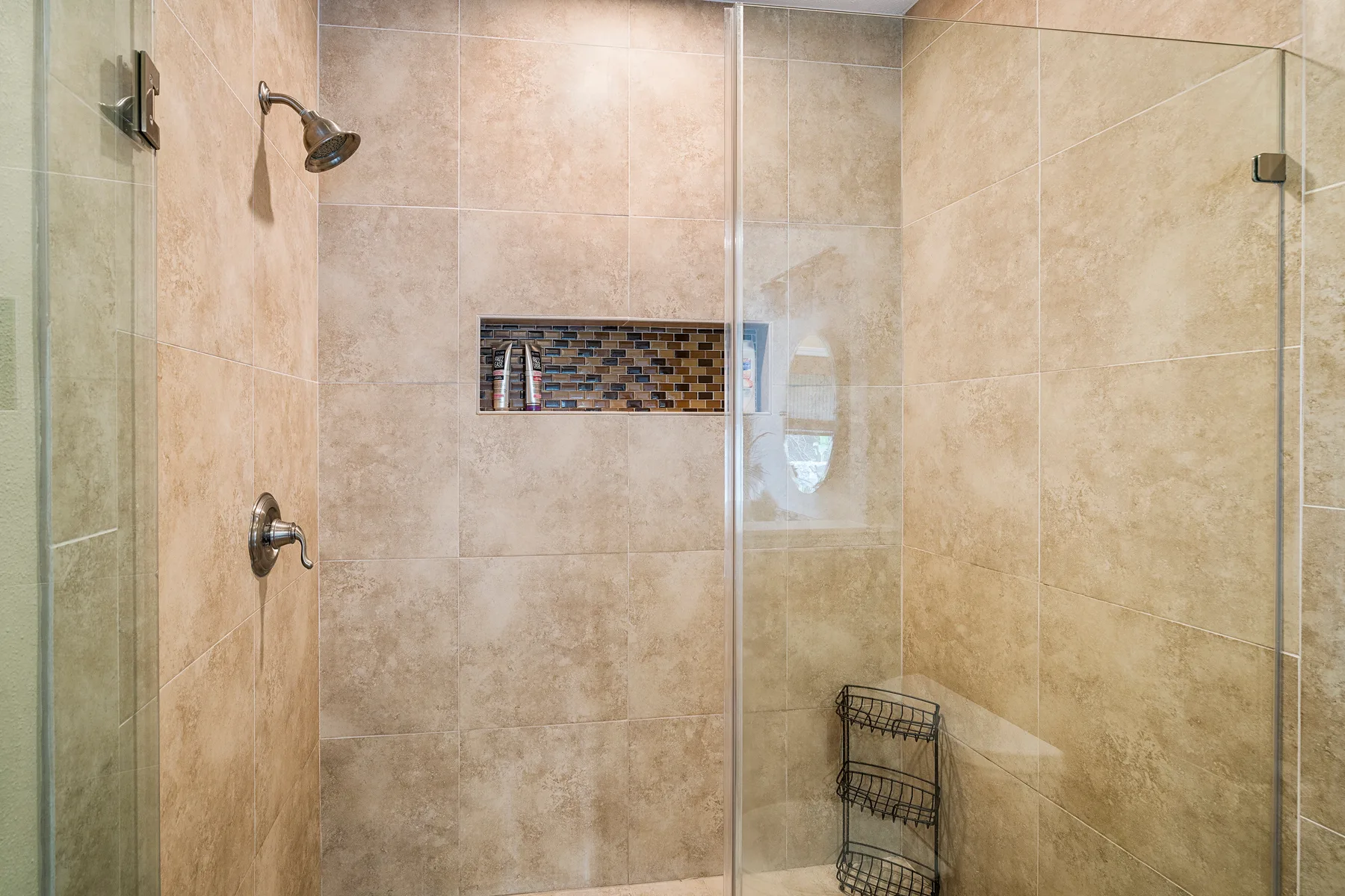 Una ducha con azulejos, paneles de vidrio y un nicho empotrado en la pared.