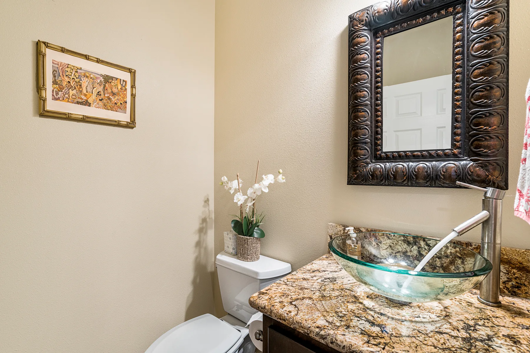 Un tocador de baño tiene un lavabo de vidrio bajo un espejo enmarcado.