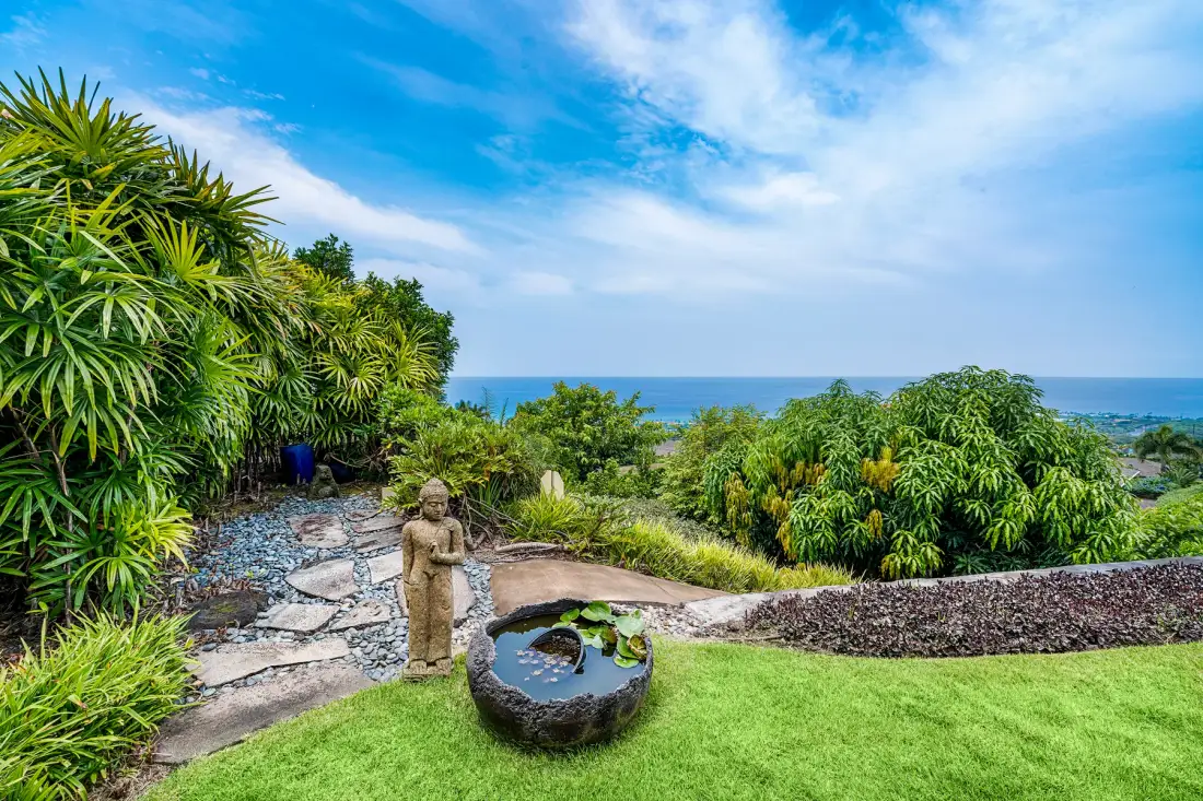 Un sendero de jardín frondoso y una fuente de agua dan al océano.