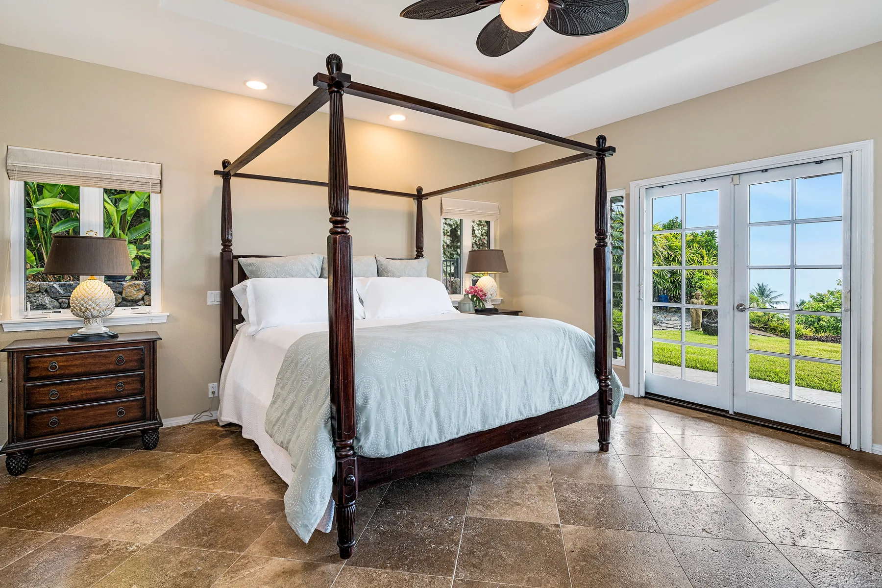 Un dormitorio con una cama con dosel junto a puertas de vidrio que dan a un jardín.