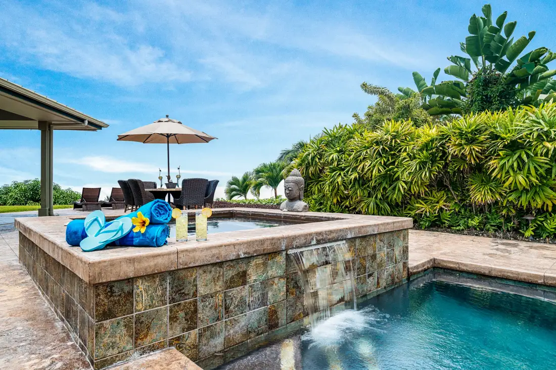 Una piscina exterior está junto a un spa elevado y una zona de estar a la sombra.