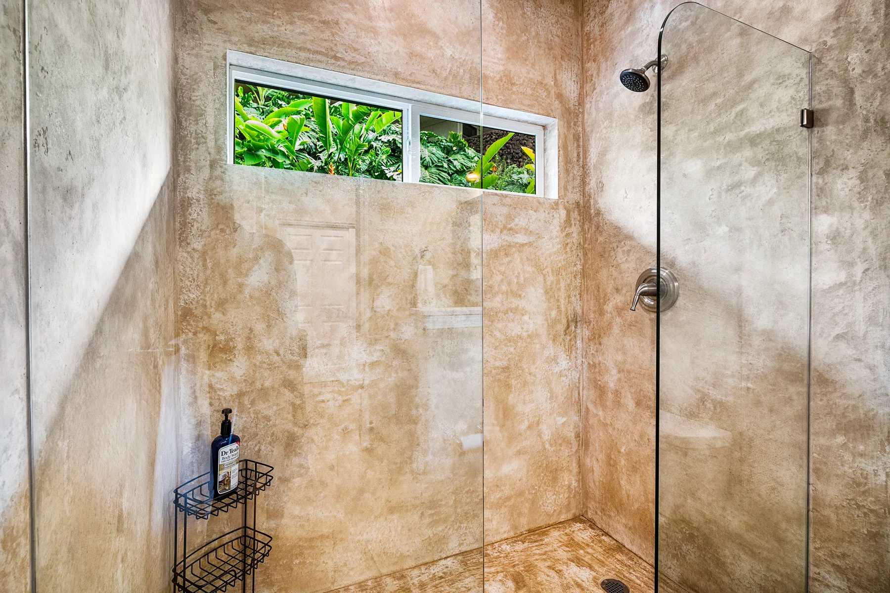 Una zona de ducha con azulejos y una pequeña ventana con vista a la vegetación.