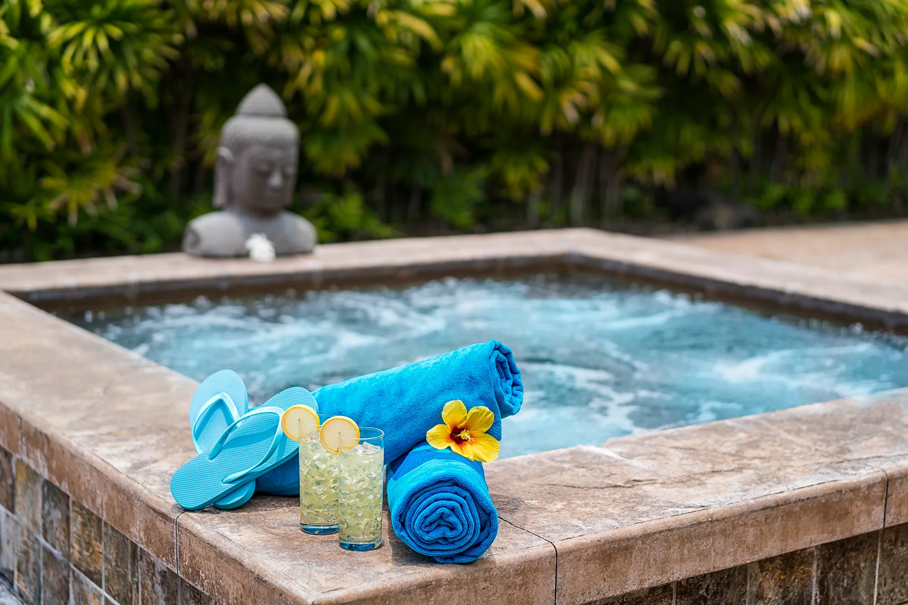 Un jacuzzi exterior burbujeante está junto a toallas enrolladas y una pequeña estatua de Buda.