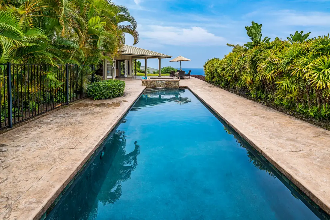Piscina al aire libre rodeada de pavimento de piedra y vegetación tropical.