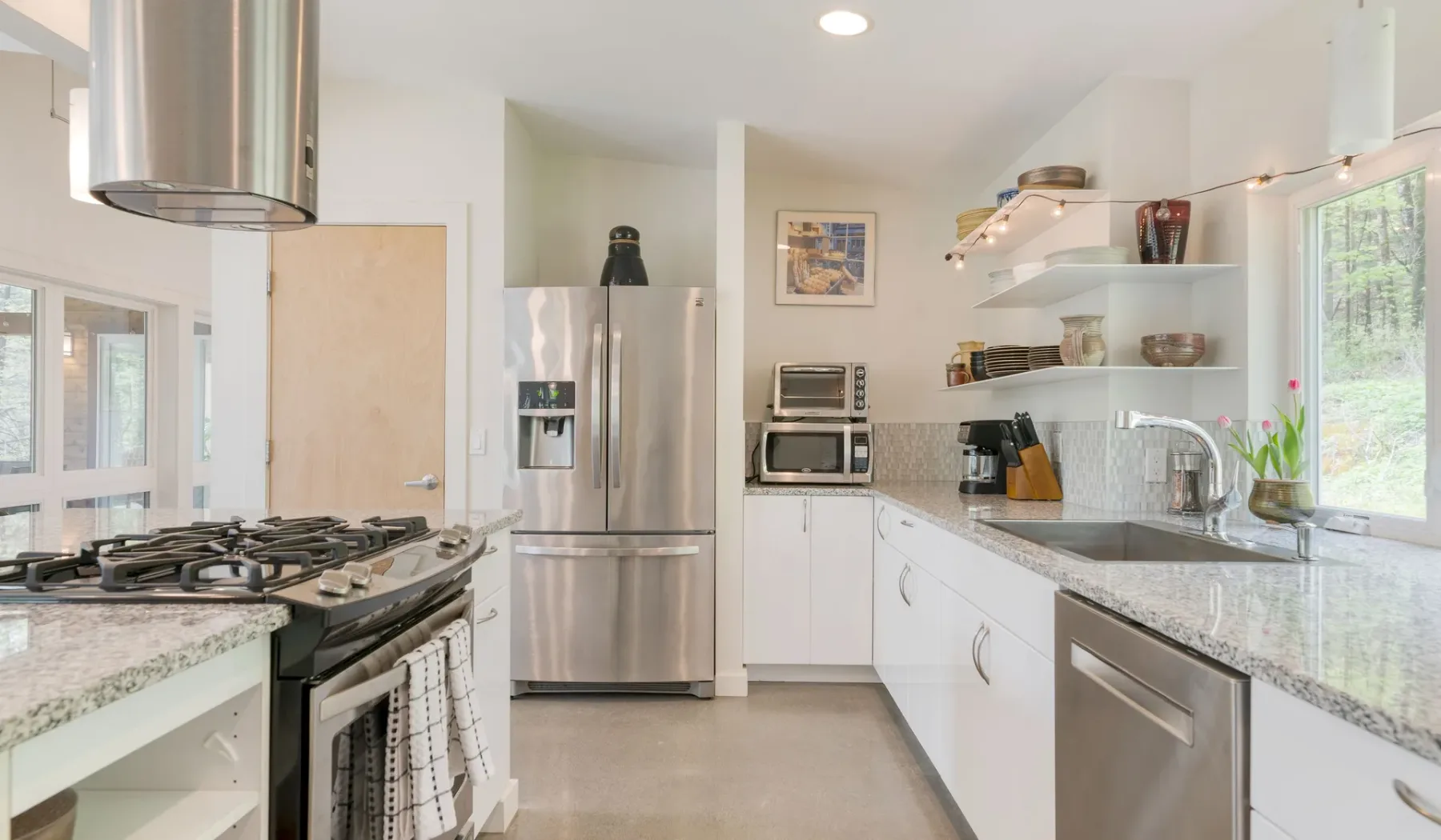 A bright kitchen with white cabinets, stainless steel appliances, and a central cooking area.