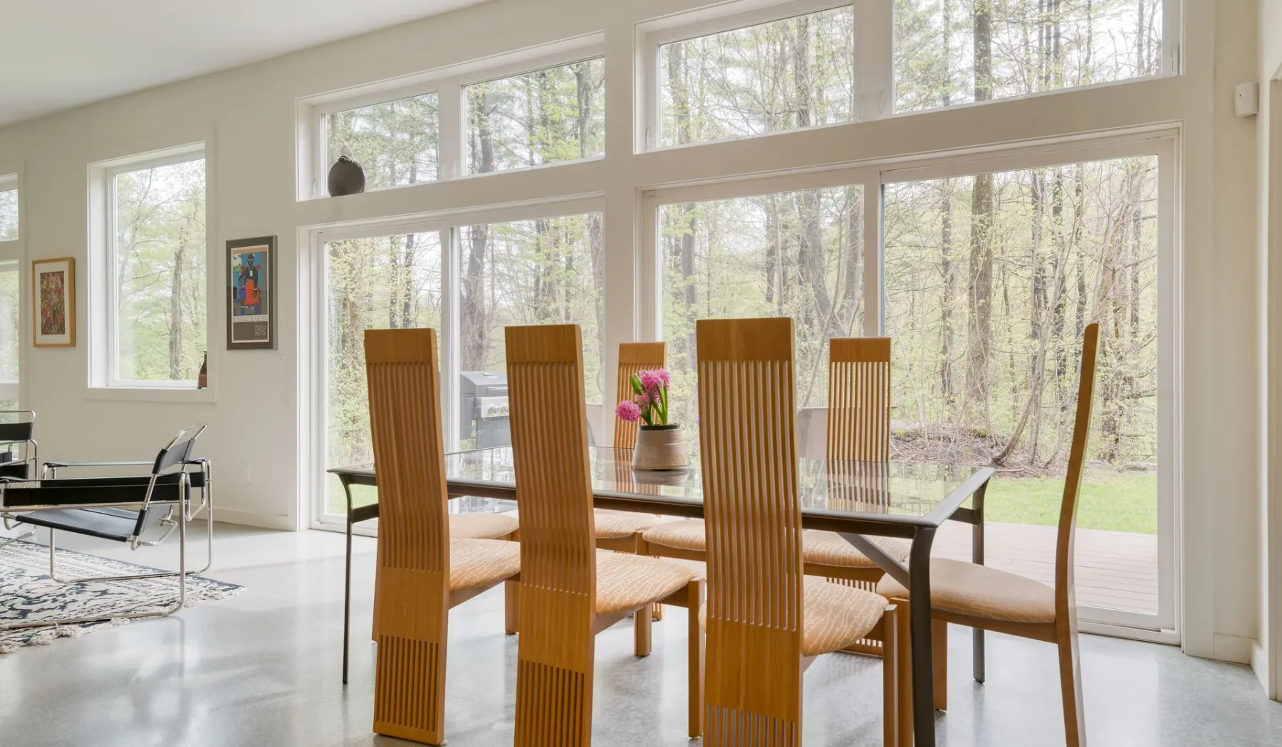 A dining area with a table and seating beside large windows overlooking trees.