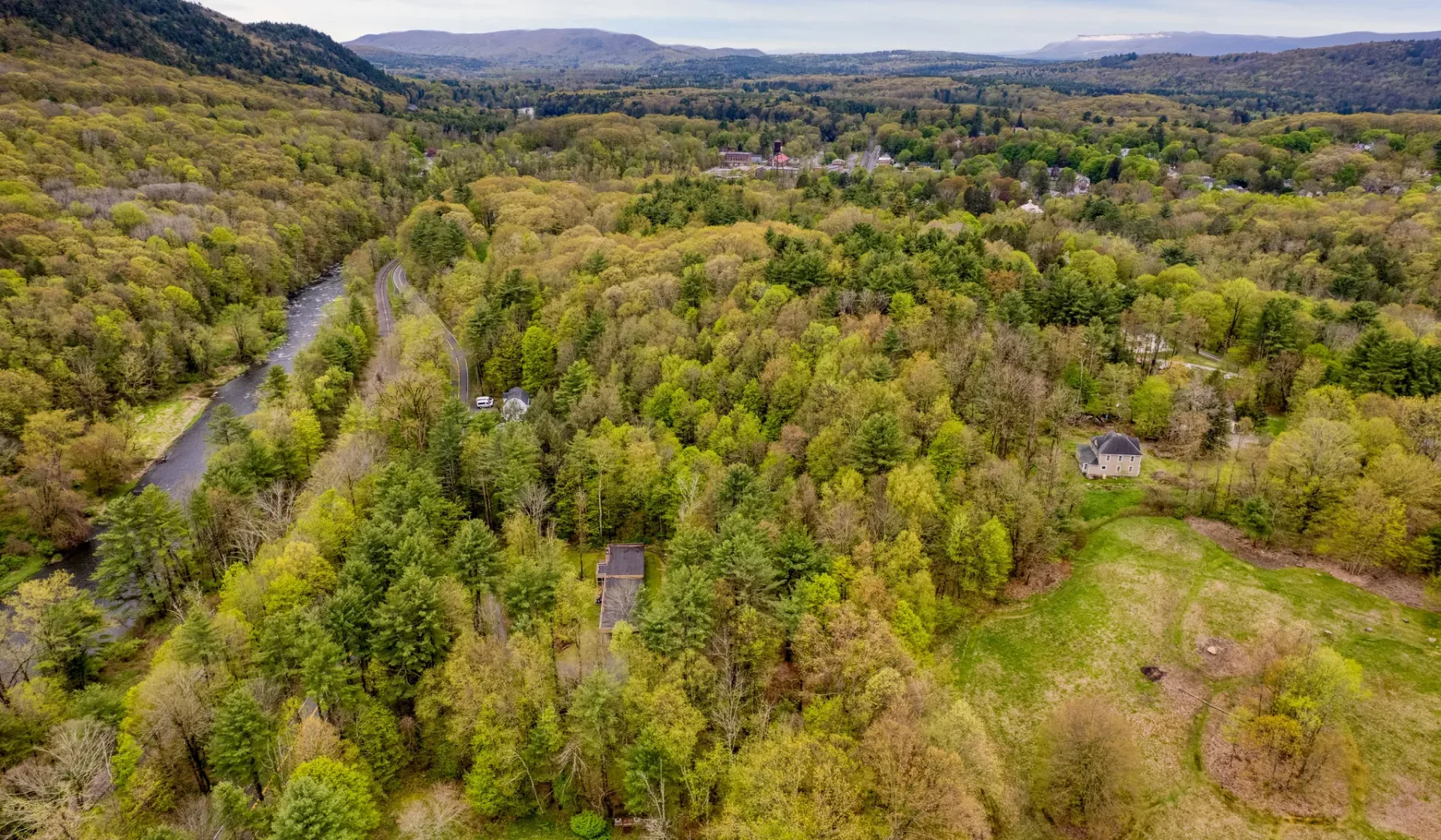 Aerial view of a wooded valley with a winding river and open meadow.