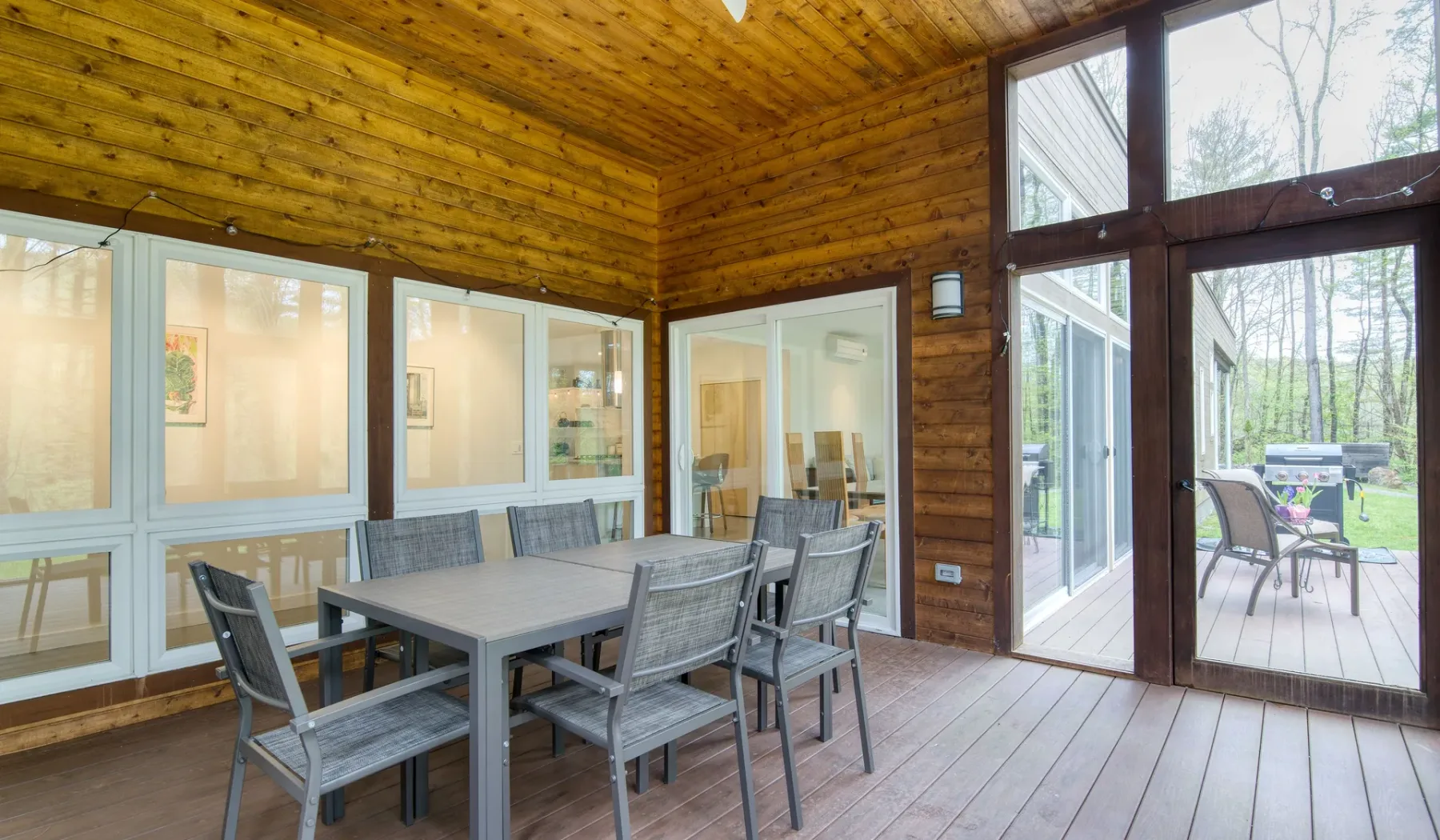 A wood-paneled dining area with a table and large windows opening onto a deck.