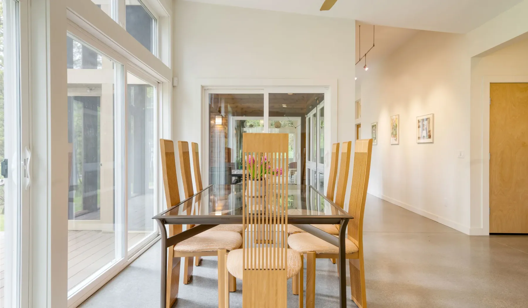 A dining area with a glass-topped table and tall windows along one side.