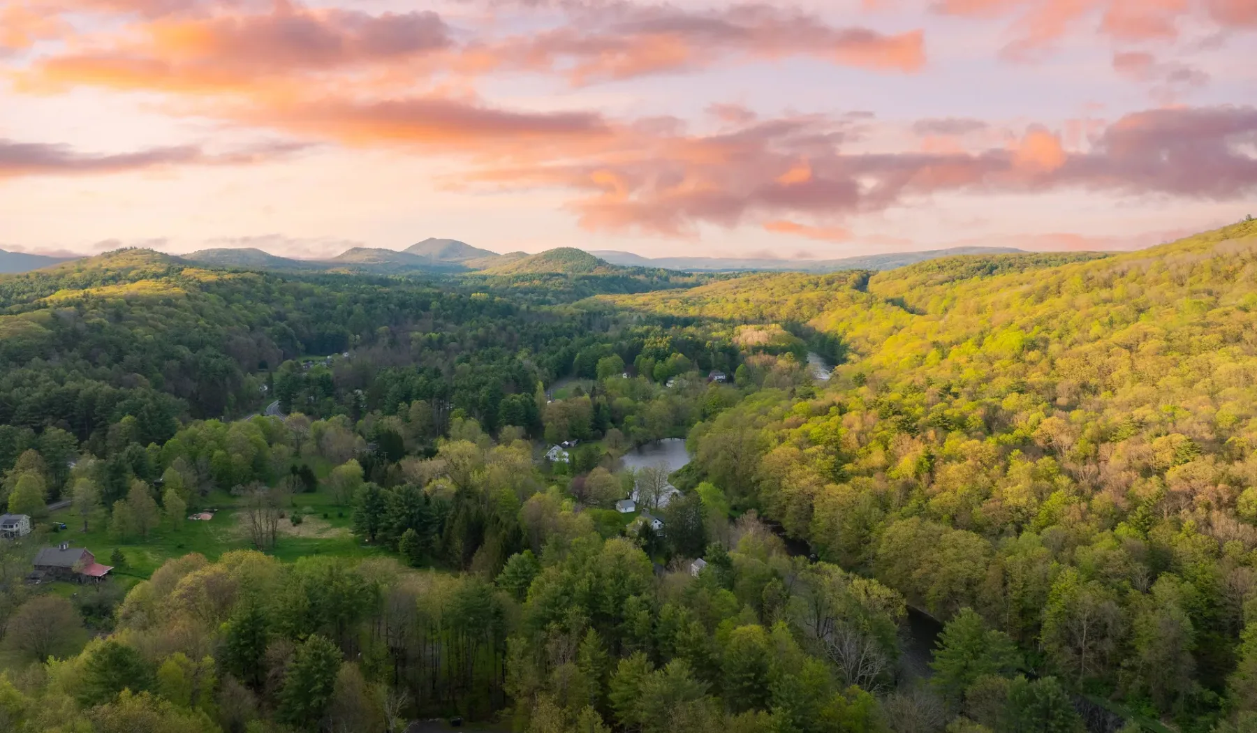 A broad forested valley stretches beneath distant hills and a colorful sunset sky.
