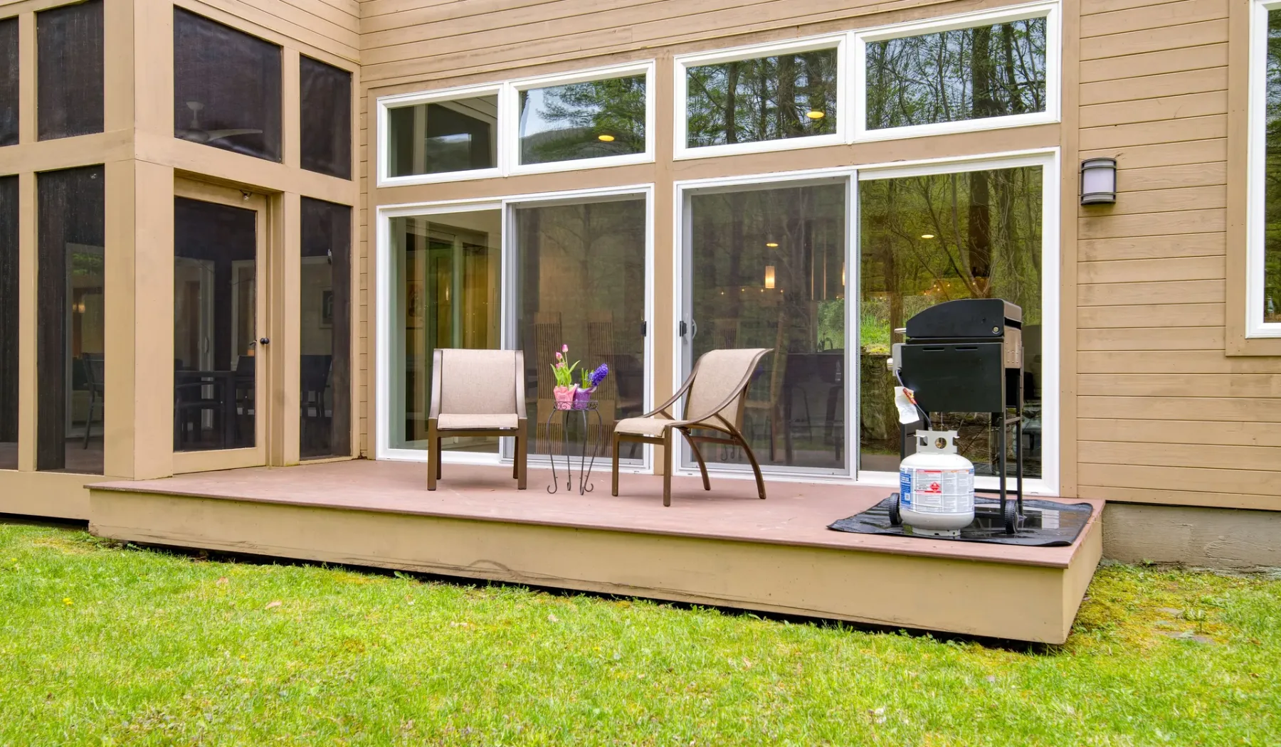 A wooden deck with outdoor seating and a grill overlooks a grassy yard.
