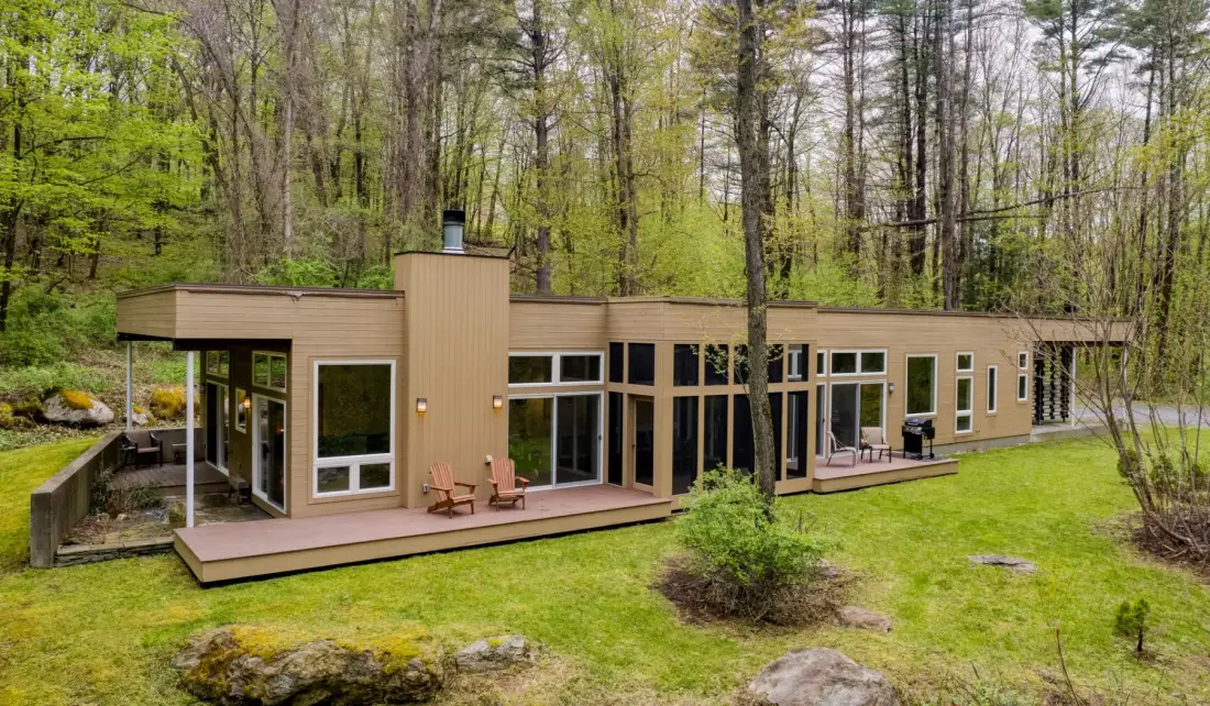 A low modern house sits among trees, with broad windows and a wooden deck.